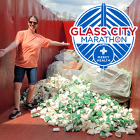 Kris Patterson stands beside a mountain of 2022 Glass City Marathon cups and pizza boxes ready to be composted.