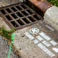 A storm drain with the stenciled message, "Drains are for rain. Flows to waterway." marked beside it.